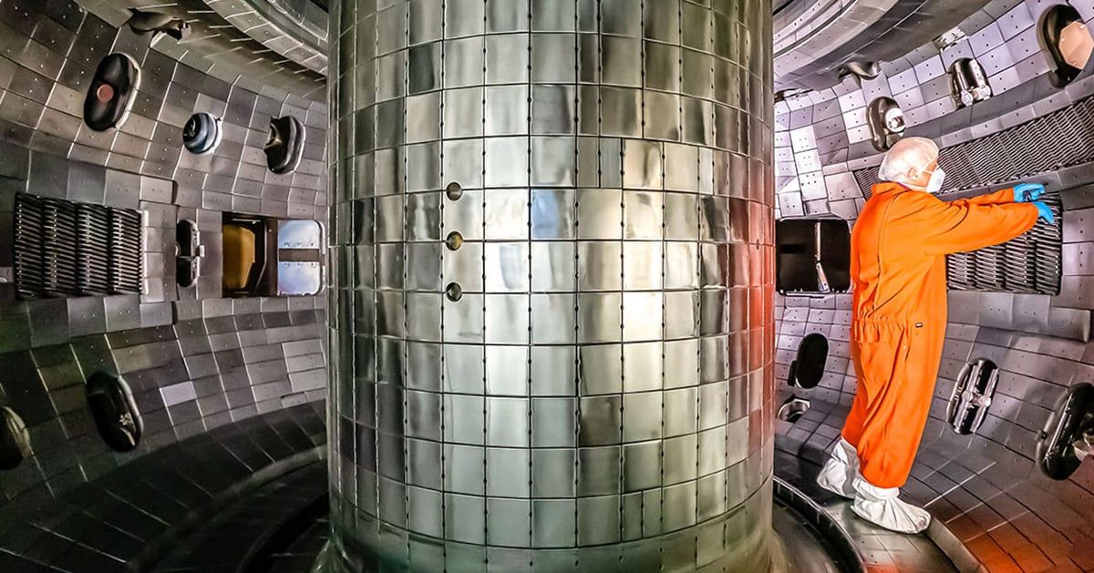 A technician works inside a tokamak, the magnetic confinement device where superheated plasma is contained for nuclear fusion experiments.
